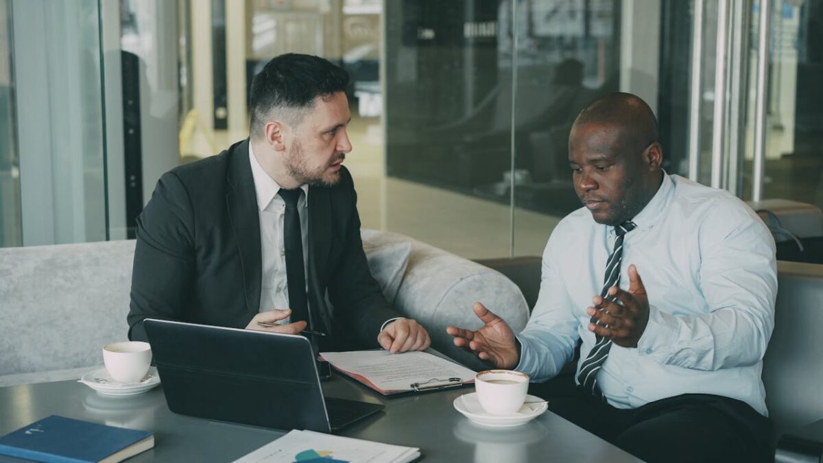 Two businessmen in discussion over coffee and laptop in modern office setting.