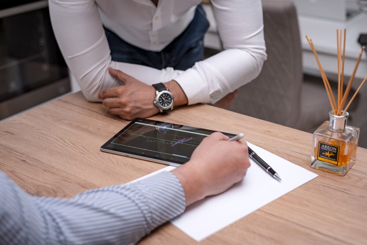 Two business professionals discuss data on a digital tablet at a wooden desk.